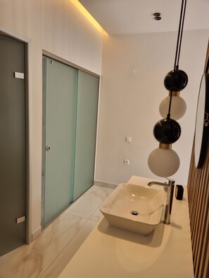 Un baño moderno con un espejo grande, una lámpara de pared y una puerta corredera de techo a piso.