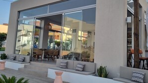 Un edificio moderno con amplios ventanales, mobiliario exterior con cojines y una escalera que conduce a la entrada.
