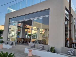 Un edificio moderno con amplios ventanales, mobiliario exterior con cojines y una escalera que conduce a la entrada.