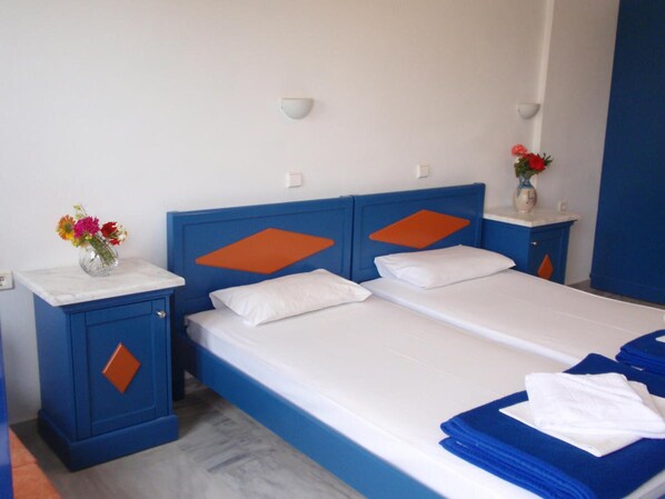 A hotel room with a double bed, a small bedside table with a vase of flowers, and a nightstand with a lamp. - Leonidas Studios & Apartments (Apokoronas)