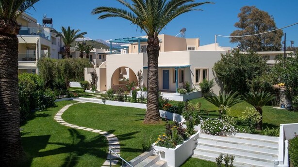 Un quartier résidentiel avec une pelouse bien entretenue, des palmiers et un escalier blanc menant à un immeuble dont le toit est bleu.
