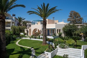 A residential area with a well-maintained lawn, palm trees, and a white staircase leading to a building with a blue roof. - Papadakis Apartments (Apokoronas)