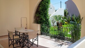 Un balcon avec une table et des chaises, une vue sur un jardin et un bâtiment blanc en arrière-plan.