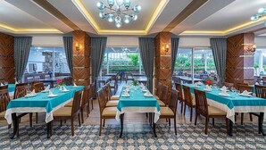 A dining area with multiple tables set for guests, featuring a patterned floor and a central chandelier. - Ramira Beach Hotel (Alanya)