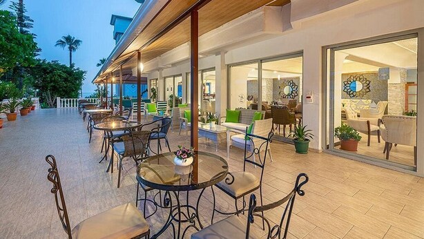 An outdoor patio area with round tables and chairs, a wooden ceiling, and glass doors leading to an interior space. - Ramira Beach Hotel (Alanya)