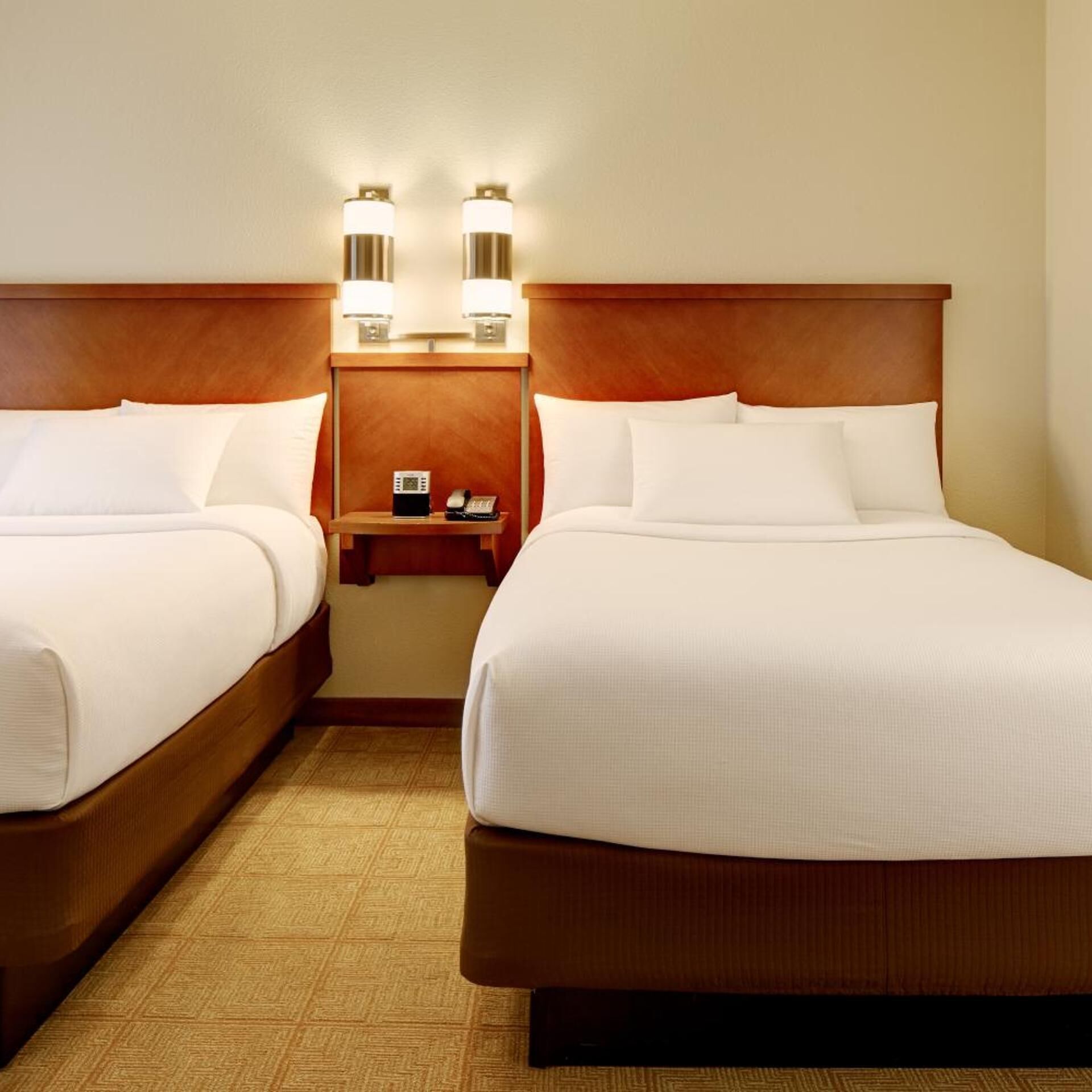 Een hotelkamer met twee bedden, een houten hoofdeinde, een nachtkastje met telefoon en lamp, en een kamerbreed tapijt met dessin.