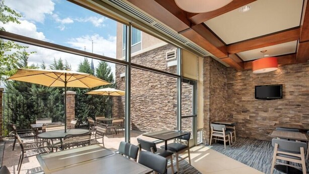 An outdoor patio with tables and chairs, large windows, and a stone wall. - Hyatt Place Reno Tahoe Airport (Reno)