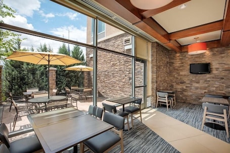 An outdoor patio with tables and chairs, large windows, and a stone wall.