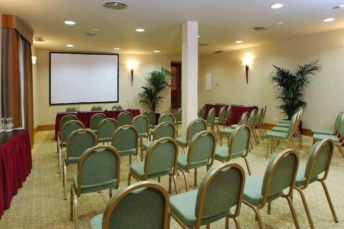Una sala conferenze con file di sedie, uno schermo per proiezioni e tavoli con tovaglie rosse.