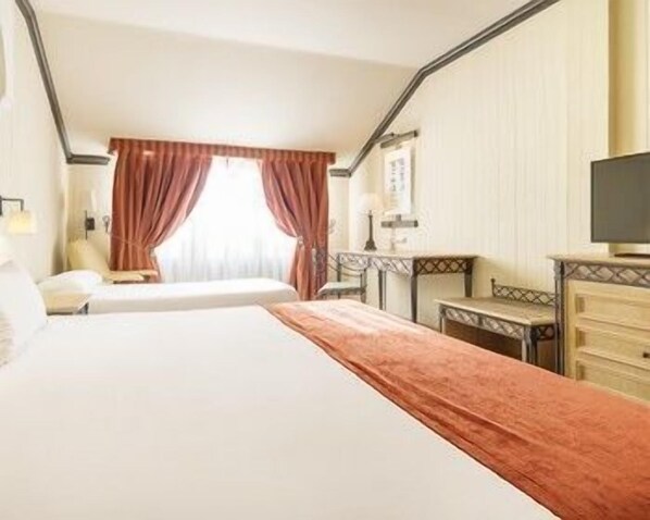 A hotel room with two beds, a desk, a chair, a television, and a window with curtains.