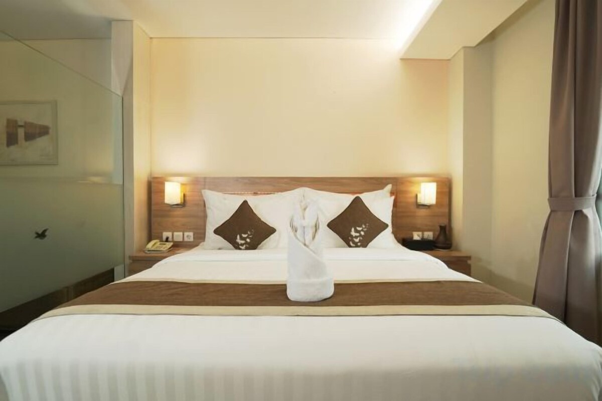 A hotel room with a neatly made bed, two bedside lamps, and a nightstand with a phone.