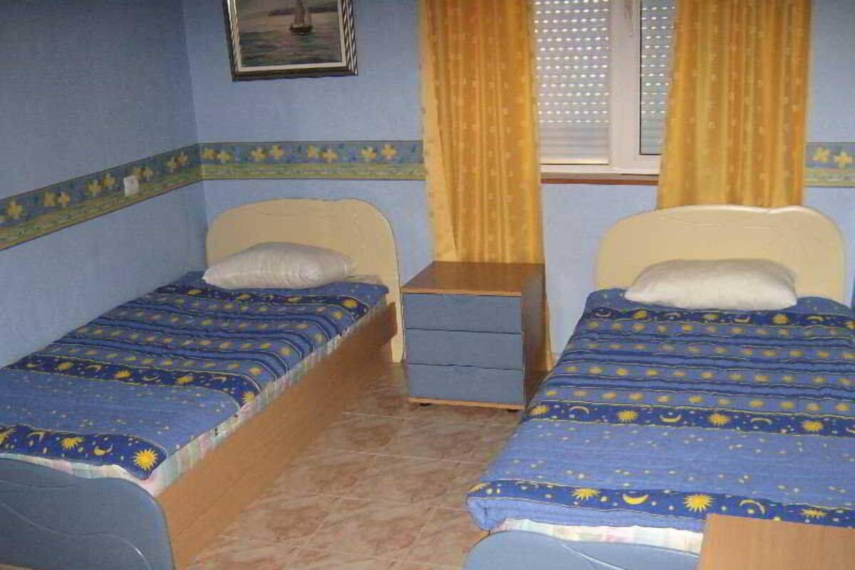 A bedroom with two single beds, a nightstand, a dresser, and a window with curtains.