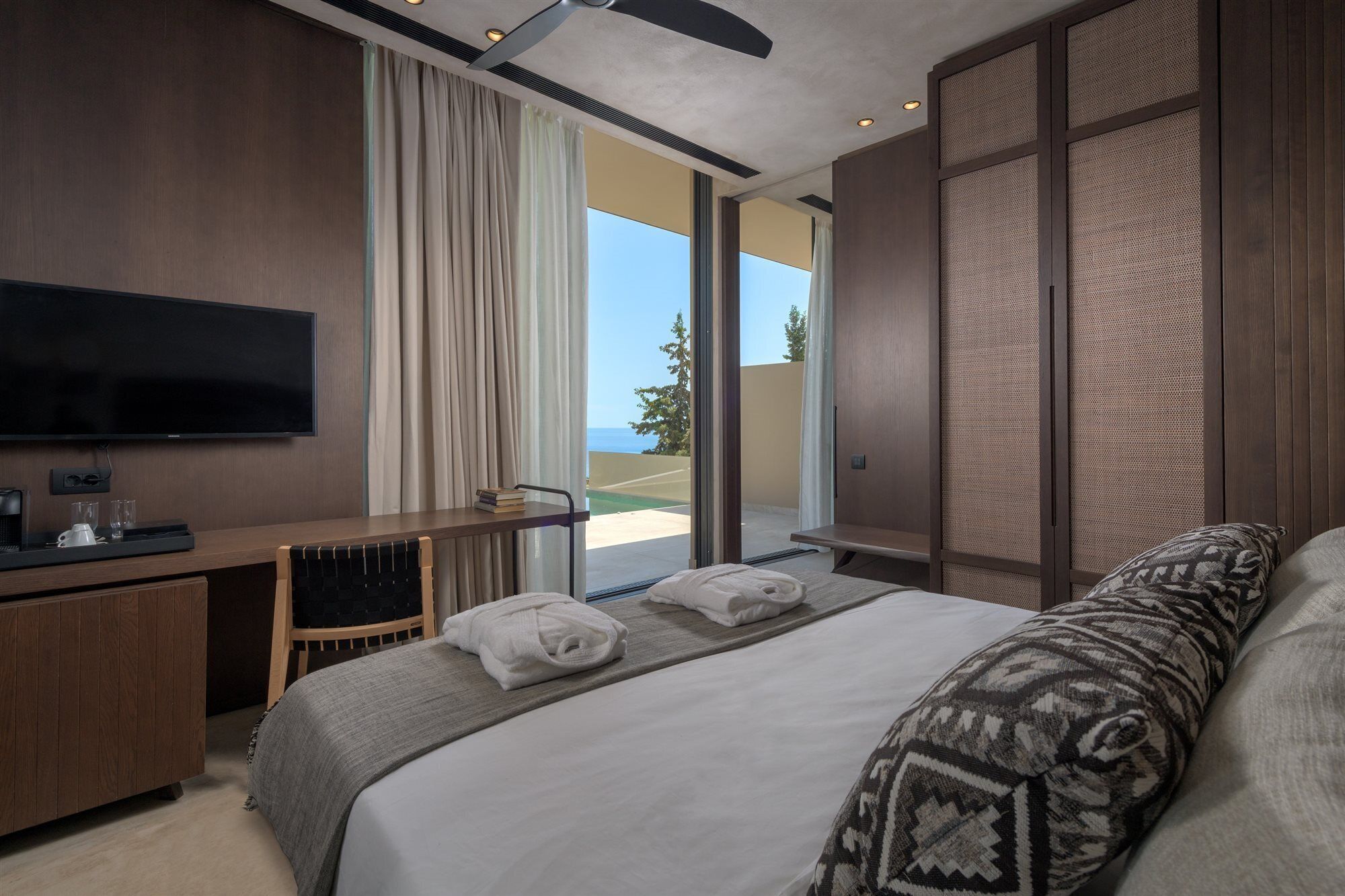 Une chambre d’hôtel moderne dotée d’un grand lit, d’un bureau avec un téléviseur à écran plat et offrant une vue sur la mer grâce à une porte-fenêtre coulissante.