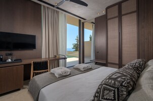 Habitación de hotel moderna con una cama grande, un escritorio con televisor de pantalla plana y vista al mar a través de una puerta corrediza de vidrio.