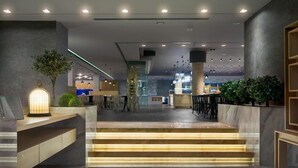 Un vestíbulo moderno con una recepción de mármol, una escalera con peldaños iluminados y una zona de estar con sillas y mesas.