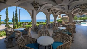 Un área de estar al aire libre con muebles de mimbre y mesas, con vistas panorámicas al mar y las colinas.