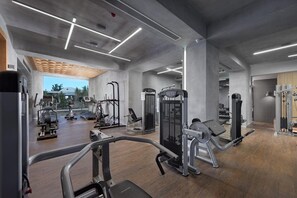 Ein modernes Fitnessstudio mit verschiedenen Trainingsgeräten, einer Holzbalkendecke und großen Fenstern.