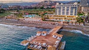 An aerial view of a coastal resort with a large hotel, a pier with sun loungers, and a pool area. - Aria Resort & Spa Hotel (Alanya)