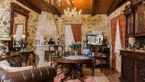 A rustic stone-walled room with a wooden ceiling, a chandelier, a round wooden table, leather furniture, and antique decor. - Casa Di Veneto (Hersonissos)