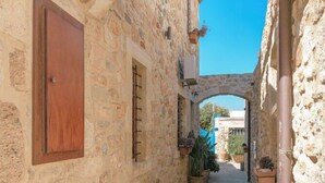 A narrow stone pathway flanked by buildings with wooden shutters and potted plants. - Casa Di Veneto (Hersonissos)