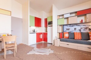 Um apartamento moderno com cozinha, sala de jantar e sala de estar, incluindo sofá e uma televisão grande presa à parede.