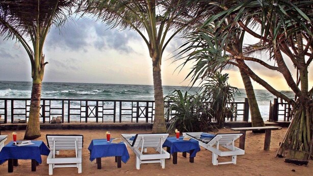 A beachside seating area with white lounge chairs and blue tablecloths, overlooking the ocean. - Dalawella Beach Resort (Unawatuna)