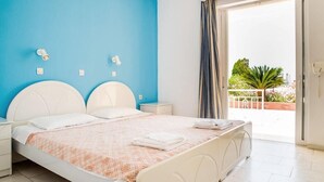 Ein Schlafzimmer mit Bett, Nachttischen, einer blauen Wand, einem Fenster mit Vorhängen und Blick auf Grünfläche.