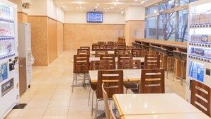 Een ruime eetruimte met meerdere tafels en stoelen, automaten en een groot scherm waarop een aanbieding wordt getoond.