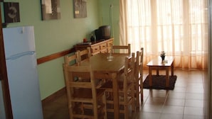 A dining area with a wooden table and chairs, a television on a stand, and a refrigerator.