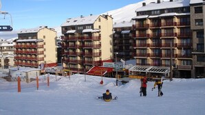 A snow-covered ski resort with multi-story buildings, including a hotel with balconies and a sign advertising "APARTMENTS PARADIS BLANC".