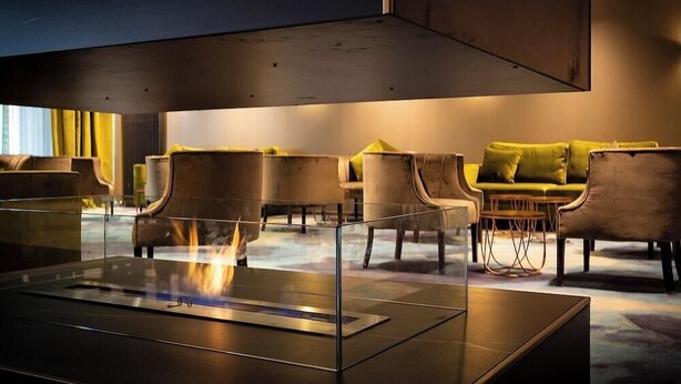 A modern lounge area with a glass-top table, comfortable seating, and a visible fire feature. - Achat Hotel Frankfurt Maintal (Maintal)