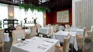 A formal dining room with multiple tables and ornate chairs, a decorative wall with a map, and a balcony with plants. - Herods Vitalis Spa Hotel Eilat (Eilat)