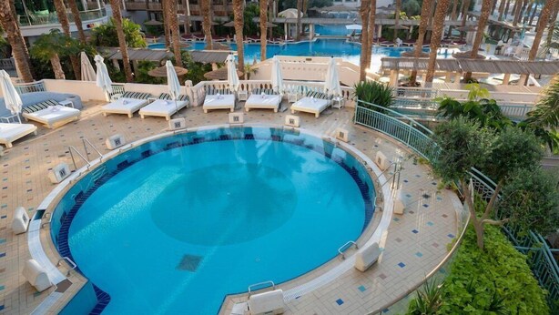 A circular pool with lounge chairs and umbrellas, surrounded by palm trees and a tiled deck. - Herods Vitalis Spa Hotel Eilat (Eilat)