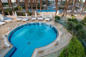 Une piscine circulaire entourée de palmiers et dotée d’une terrasse carrelée, avec des chaises longues et des parasols.
