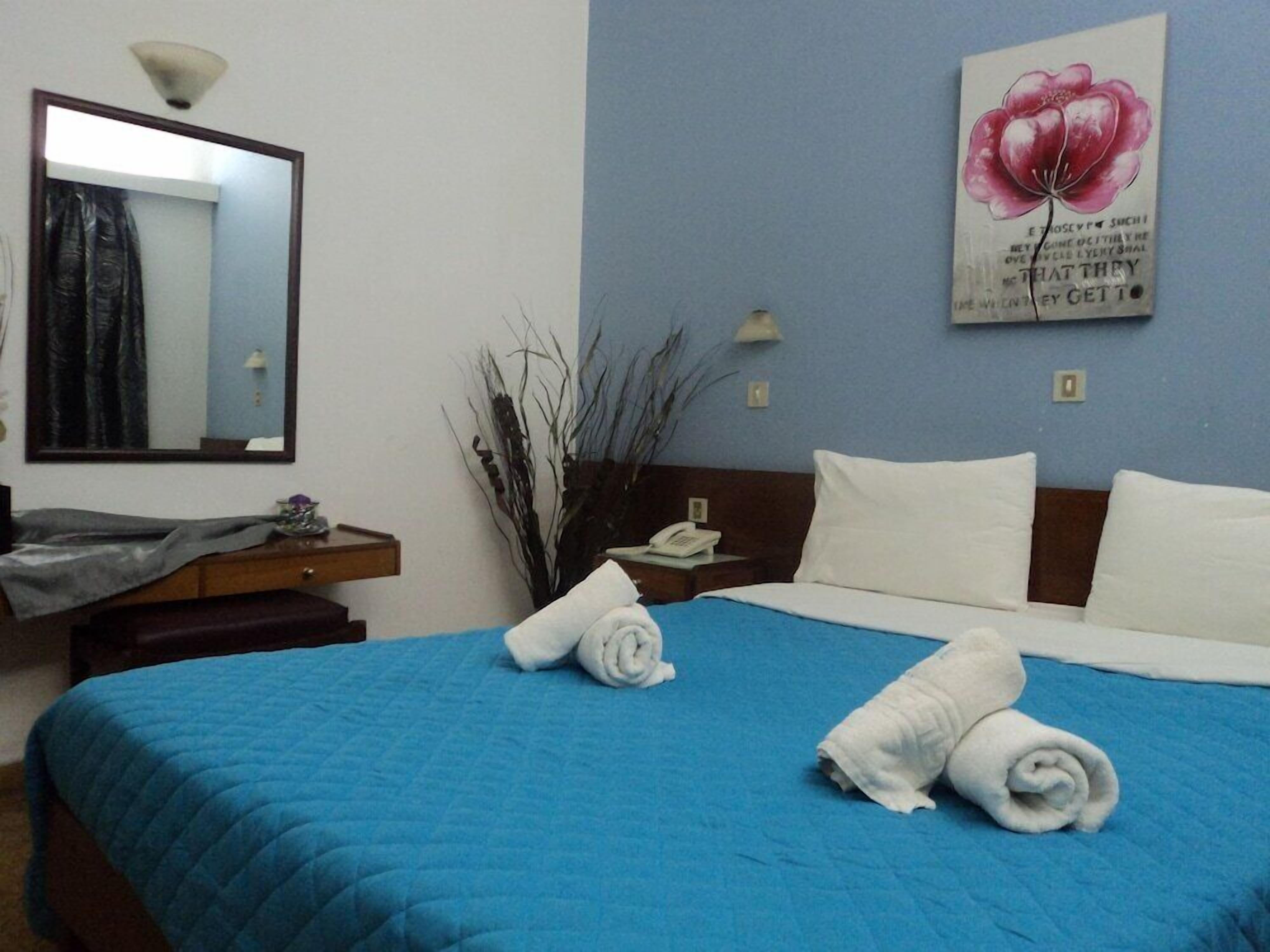 Een hotelkamer met een groot bed, een nachtkastje met een lamp, een spiegel en een wand met een bloemschilderij.
