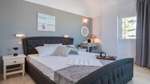 A bedroom with a large bed, bedside tables, a nightstand, a lamp, a clock, and a window with curtains. - Pasiphae (Heraklion)