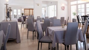 A spacious dining area with multiple tables and chairs, large windows allowing natural light, and a modern interior design. - Pasiphae (Heraklion)