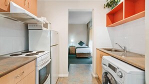 A compact kitchen with a stove, oven, and washing machine, leading to a bedroom with a bed and nightstand. - Comfort Inn and Suites Lakes Entrance (Lakes Entrance)