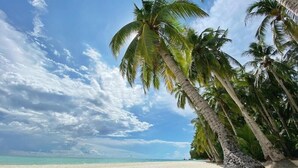 A beach with white sand and palm trees under a partly cloudy sky. - Jonys Beach Resort (Boracay Island)