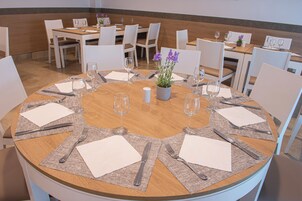 Una mesa de comedor redonda con un arreglo floral central, rodeada de sillas blancas y dispuesta con copas de vino, cubiertos y servilletas.
