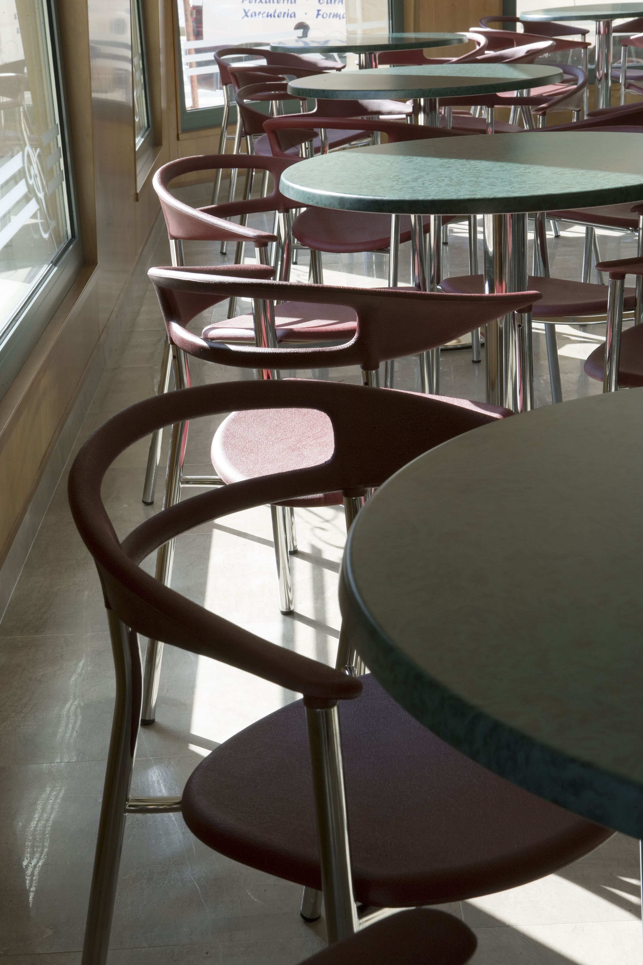 A restaurant interior with round tables and red chairs, large windows, and a tiled floor.