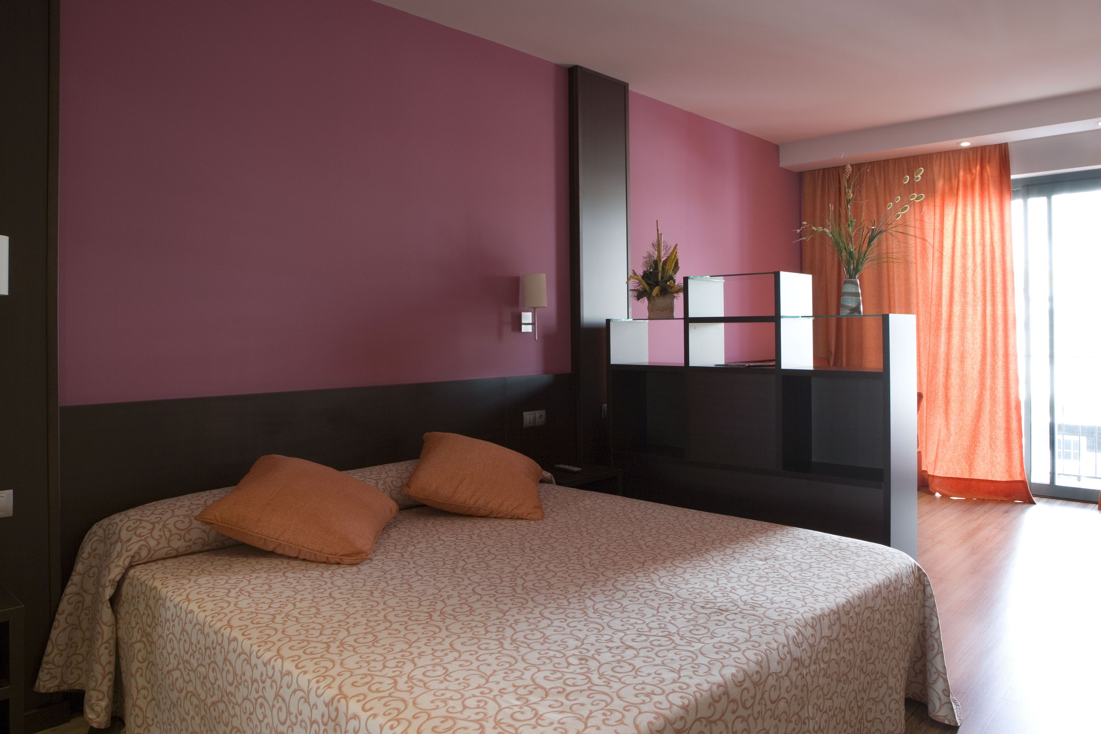 Ein Hotelzimmer mit Bett, Fernseher, Pflanze und einem Fenster mit Vorhängen.
