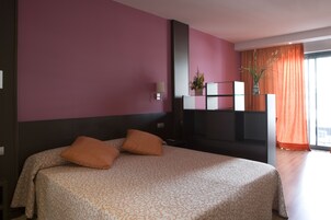 Una habitación de hotel con cama, televisión, planta y ventana con cortinas.