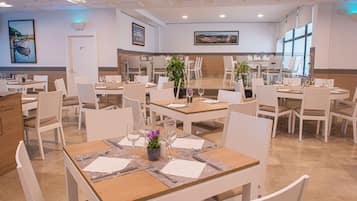 Un restaurant doté de nombreuses tables, de chaises et offrant une vue sur la ville grâce à de grandes fenêtres.