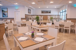 A restaurant with multiple tables, chairs, and a view of the city through large windows.