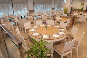 A spacious dining area with multiple round tables, each set with white chairs and a central vase. - Loar Ferreries (Ferreries)