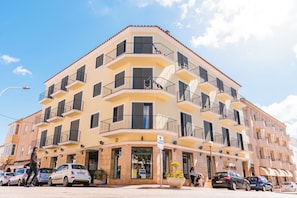 A multi-story building with balconies, a ground-floor entrance, and parked cars.