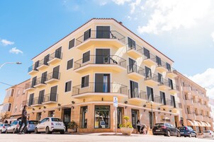 Un edificio de varios pisos con balcones, entrada a nivel de calle y automóviles estacionados.