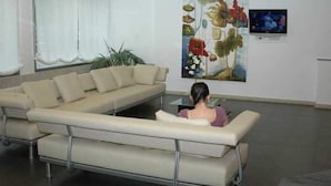 A modern waiting area with a sofa, a coffee table, and a painting of flowers on the wall. - Nuevo Villa Juanita Hotel (O Grove)