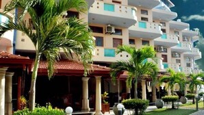 Un hotel de varios pisos con balcones, palmeras y una entrada con techo rojo.